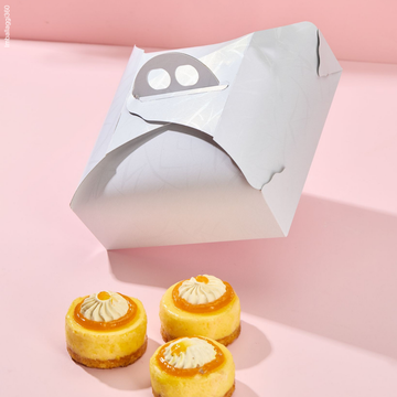Scatola porta torte bianca in movimento come se cadesse. chiusa e 3 pasticcini di fronte